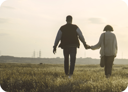 A couple holding hands and walking towards a sunset in a field.